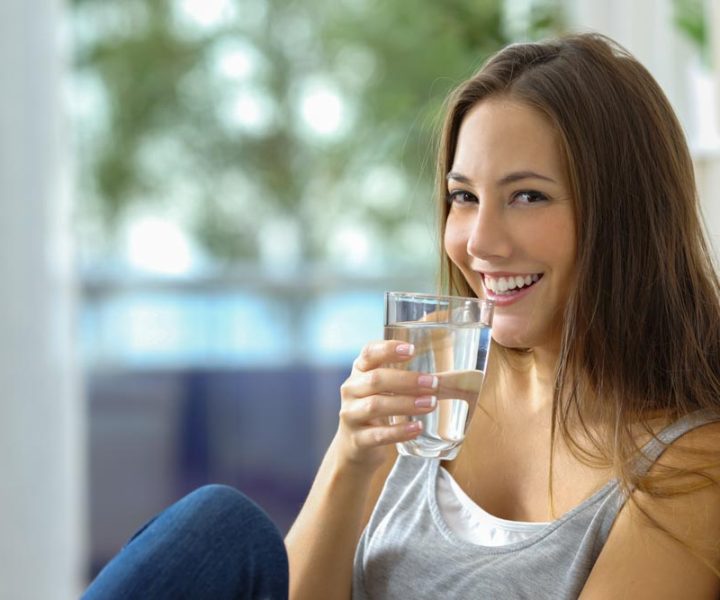 Girl drinking water sitting on a couch at home and looking at camera